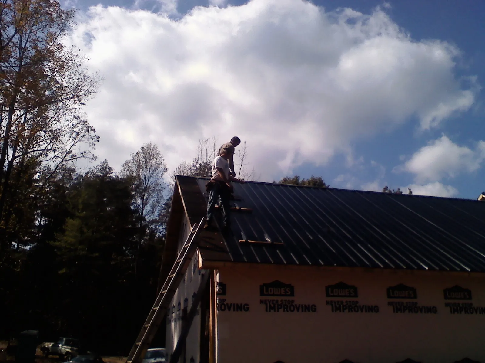 Roofer fastening dark metal panels high against a cloudy sky, from a Roof Inspection job in Malden On Hudson