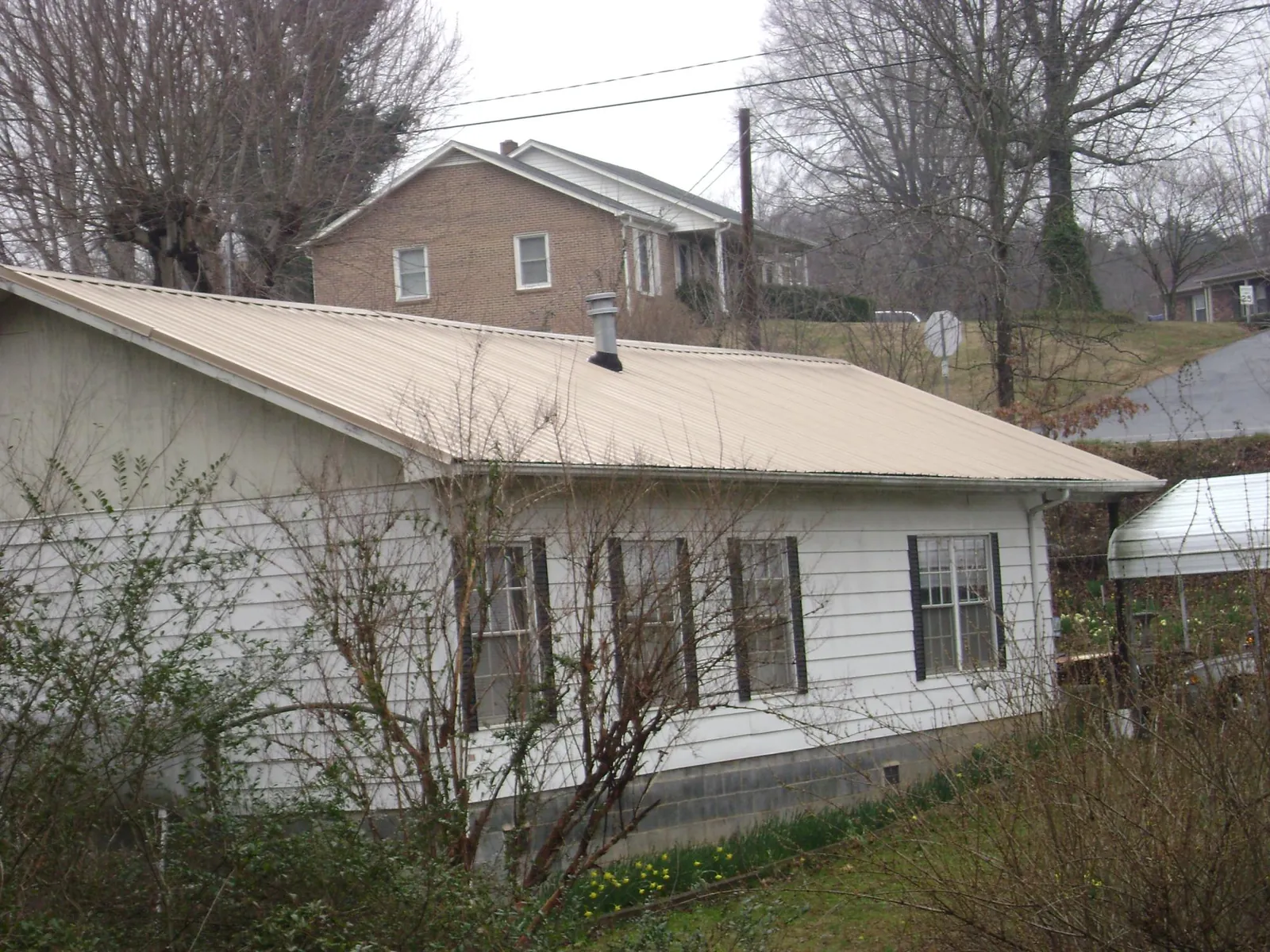 Tan metal roof on a white sided house set into a hillside — Commercial Roofing by Roofing Brothers in Malden On Hudson